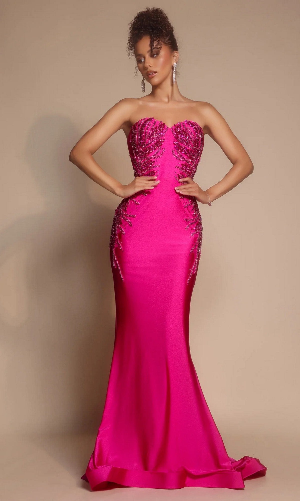 A woman poses against a plain beige background wearing the Portia and Scarlett PS26331E long formal dress in hot pink, featuring a strapless sweetheart neckline, beading, and a slight mermaid silhouette.